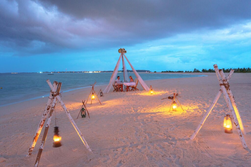 Beautiful beach dinner setup with lanterns glowing on a serene coastline during twilight.